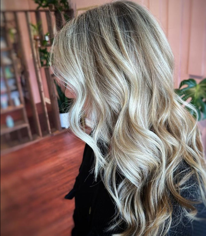 Close-up of a person with long, wavy blonde hair cascading over their shoulder. The background is softly focused, creating a warm, cozy atmosphere.