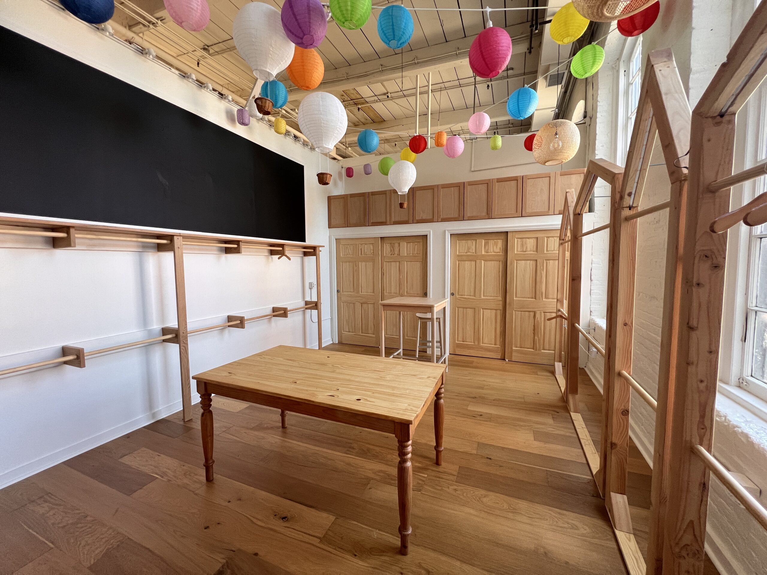 A staged, move-in-ready space with wood clothing racks, a farmhouse table and paper lanterns