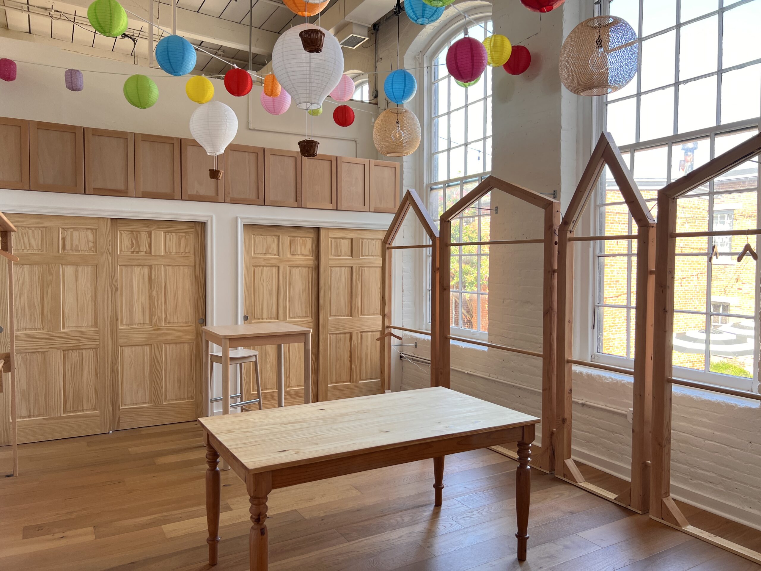 A staged space with a farmhouse table, house-shaped racks and large historic mill windows